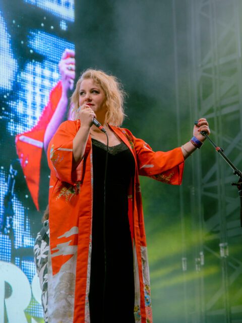 Amy Millan of the band Stars singing on stage. She is wearing a red kimono with a black dress underneath and looking away from the camera