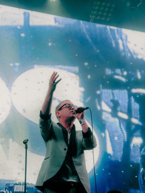 Torquil Campbell of the band Stars singing on stage. Behind him there is a screen that says Stars in bright white letters and blue lights.