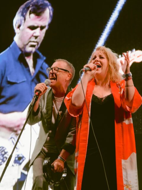 Torquil Campbell and Amy Millan of the band Stars singing together on stage. They are leaning against each other and singing passionately.