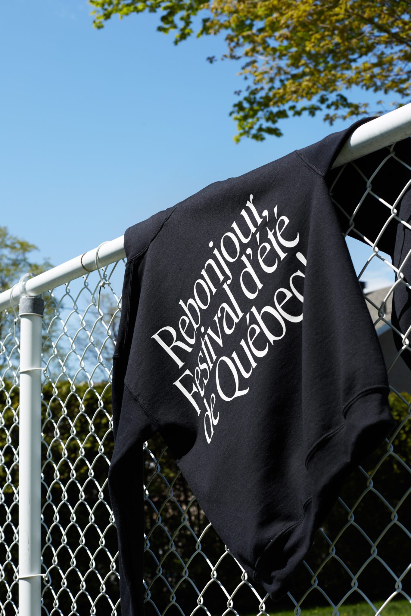 FEQ black sweater hanging on a fence. The sweater says Rebonjour on it.