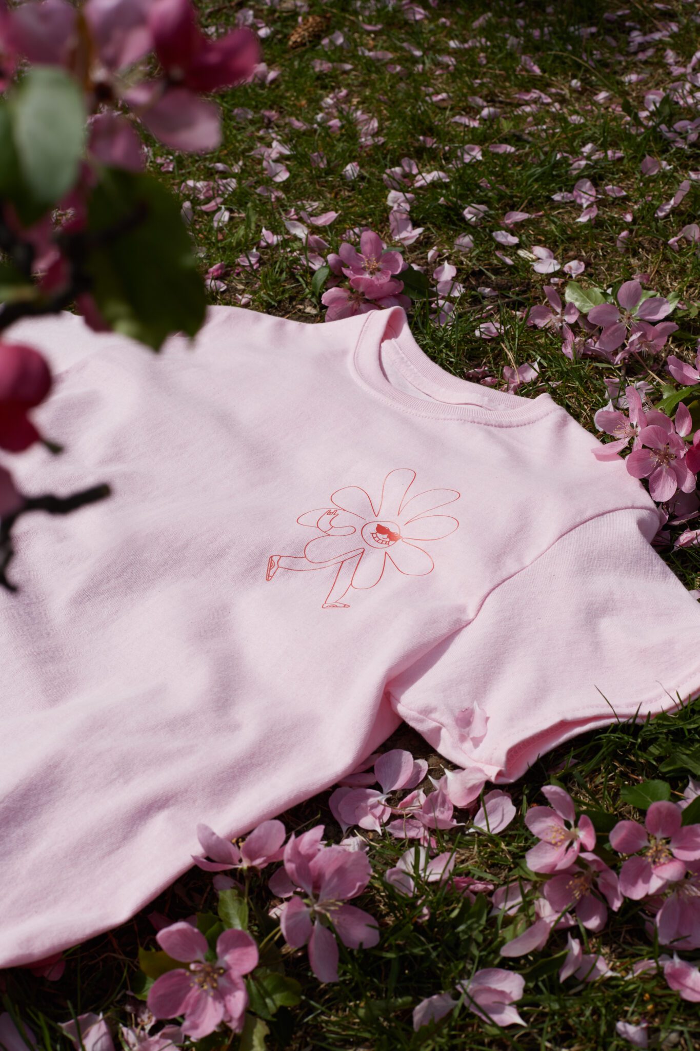 FEQ pink t-shirt with a pink flower doodled on the upper right side of the t-shirt. The shirt is on top of a field of pink petals.