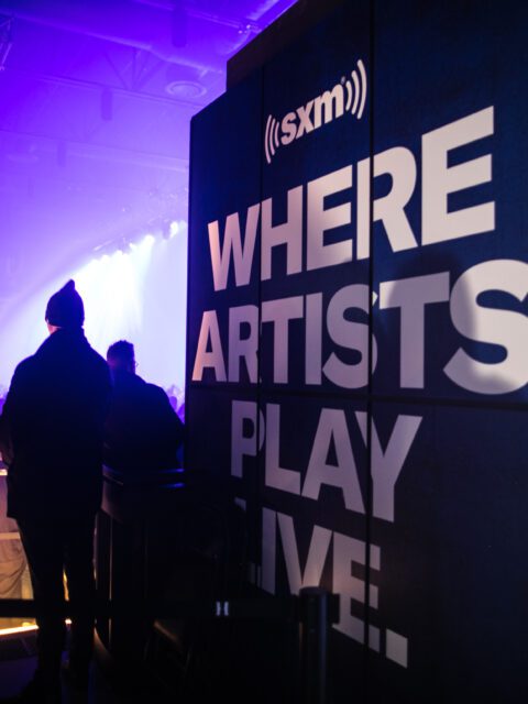 A photo of a SiriusXM sign at a concert. The signs says "Where artists play live" in white text and black background